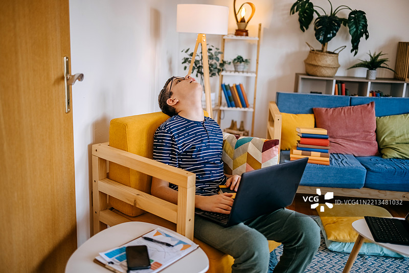 年轻的少年在家中沙发上学习，抬头思考。图片素材