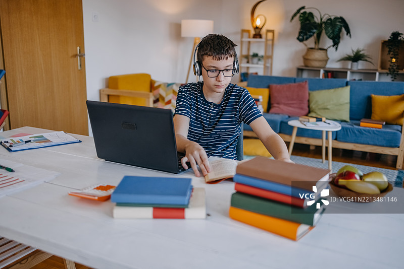 年轻的少年在家学习，使用笔记本电脑参加在线讲座图片素材