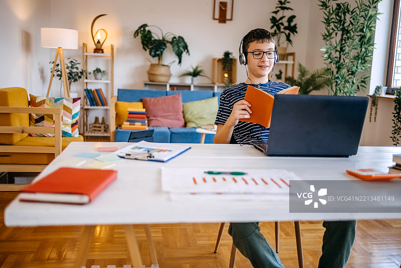 年轻的少年在家学习，使用笔记本电脑上网课，面露积极的情绪。图片素材