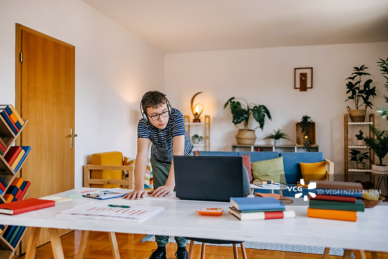 年轻的少年在家学习，站在餐桌前使用笔记本电脑上网课。图片素材