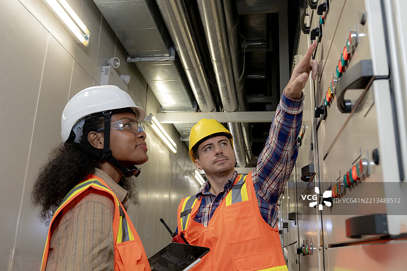 确保运营可靠性，两名工程师在设施控制室监控和维护电气基础设施。图片素材