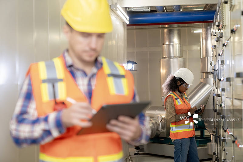 确保运营可靠性，两名工程师在设施控制室监控和维护电气基础设施。图片素材