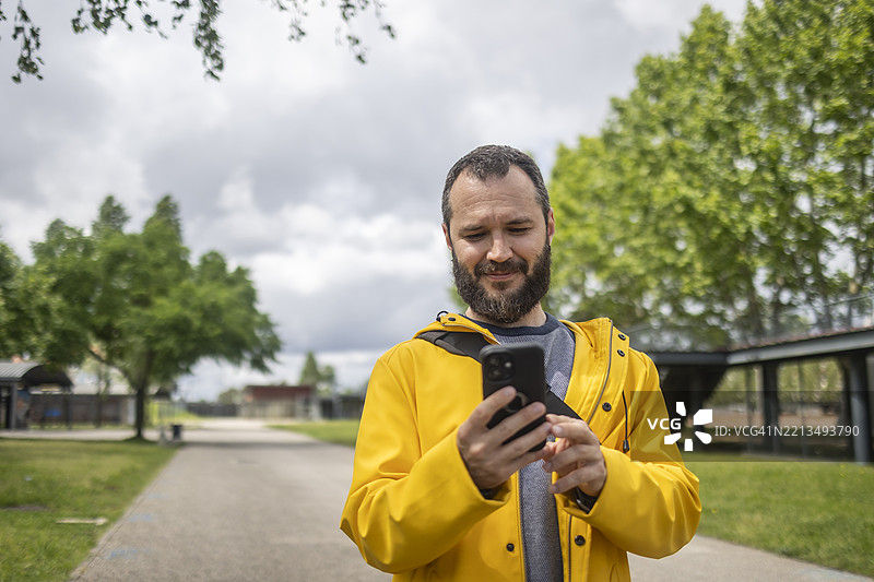 穿着黄色夹克的白人男性在公园里使用智能手机图片素材
