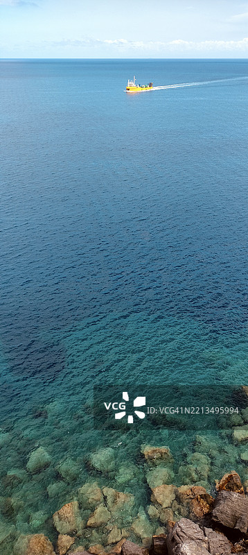 高角度视图的海岸线，岩石和礁石，背景中有一艘船图片素材