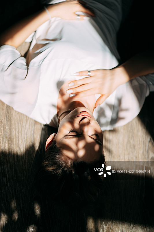 安静的女人躺在木地板上，脸上洒满了树叶的阴影图片素材