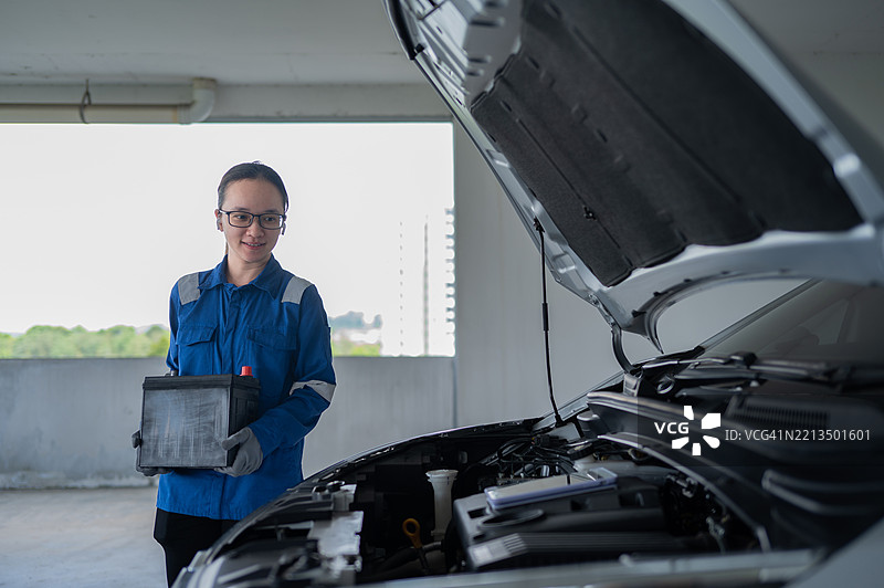 亚洲华裔年轻女性车间技师手持新电池准备更换旧电池的库存照片图片素材