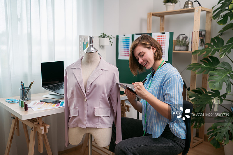 微笑的年轻时装设计师在她的工作室里做笔记图片素材