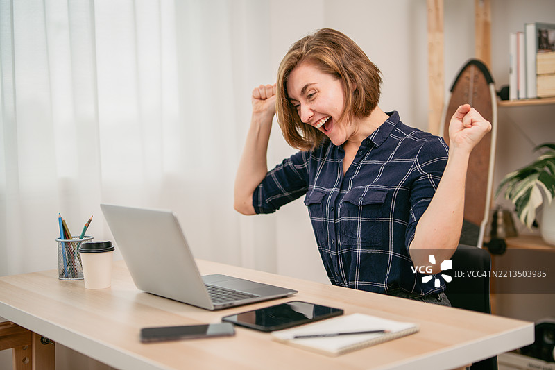 快乐的年轻女性在家中工作空间庆祝成功图片素材