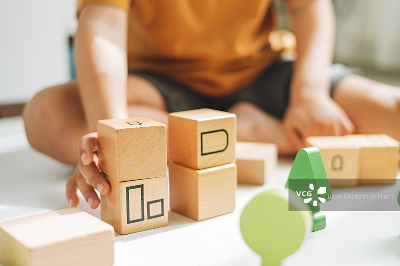 一个孩子的手小心翼翼地堆叠着带有字母和形状的木块，进行创意游戏。图片素材