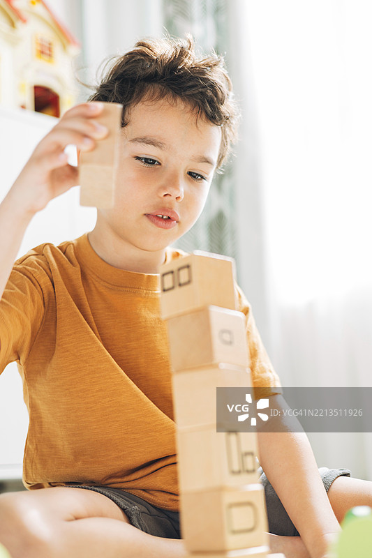 一个孩子专注地往他正在搭建的塔上添加另一块木块。图片素材