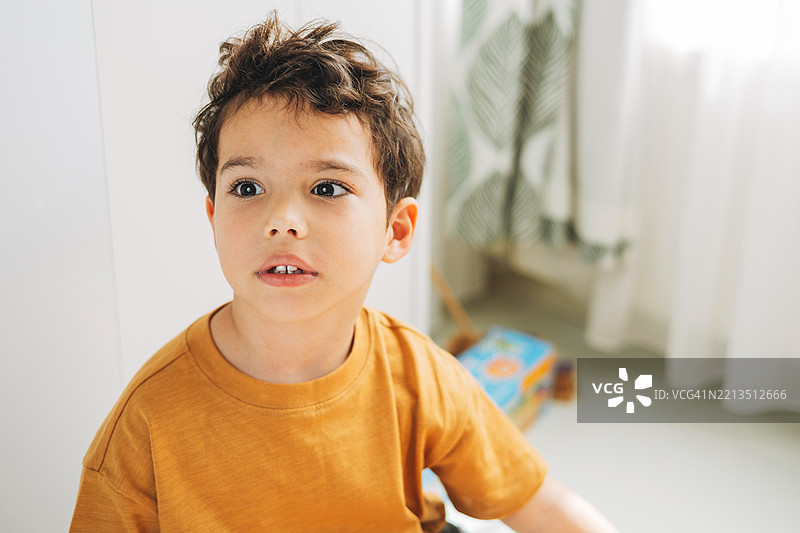 一个好奇的小男孩，棕色的头发，专注地看着某样东西，沐浴在柔和的光线中。图片素材