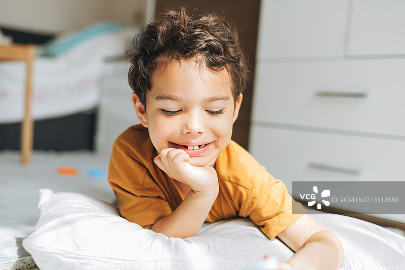 一个快乐的男孩躺在枕头上，闭着眼睛微笑，享受着宁静的时刻。图片素材