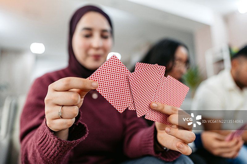 年轻穆斯林女性与朋友们在沙发上玩牌图片素材