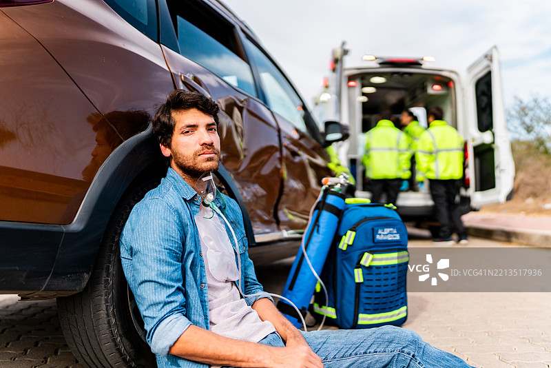 受伤的年轻男子坐在户外的地上，刚经历了车祸。图片素材