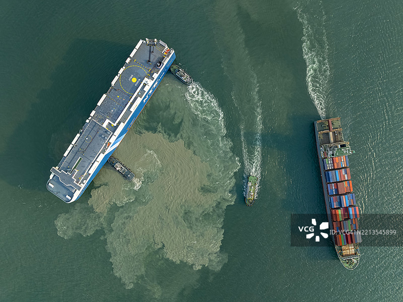 航拍视角，拖船正在将汽车运输船推入港口，集装箱船则驶出国际港口。这是关于海洋货物进出口业务的场景。图片素材