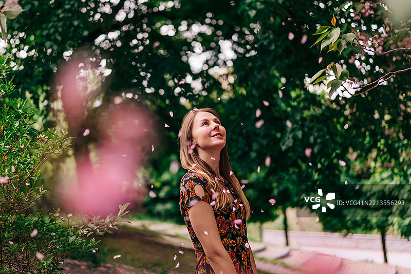 女人在郁郁葱葱的花园中享受花瓣飘落的美好时刻图片素材