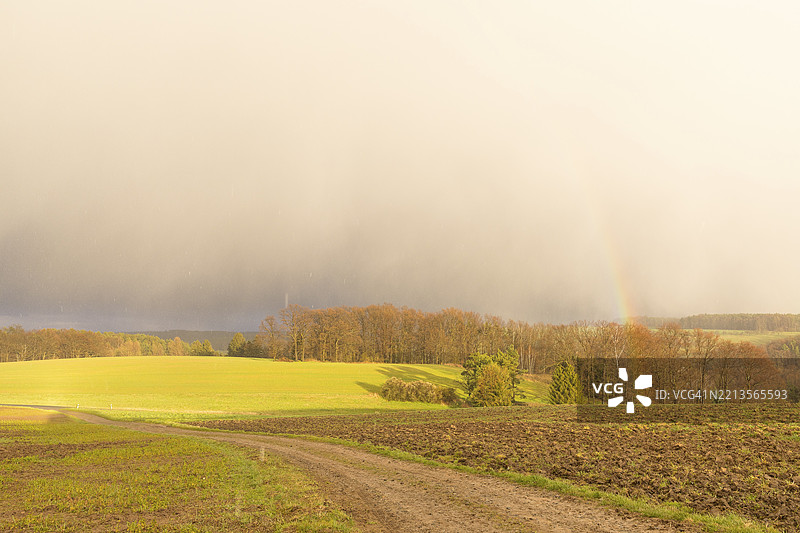 德国图林根州赫姆斯多夫附近的田野上，暴风雨伴随着雨水和阳光，以及一道彩虹。图片素材