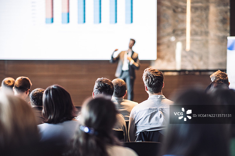 在商业活动的会议厅中，演讲者正在发言，背面是一些无法辨认的人群。图片素材