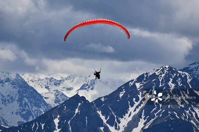 男子在德国的雪山上空滑翔伞飞行，背景是蓝天。图片素材