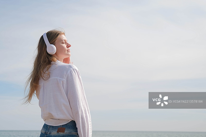 在海滩上戴着白色耳机的女性听音乐图片素材