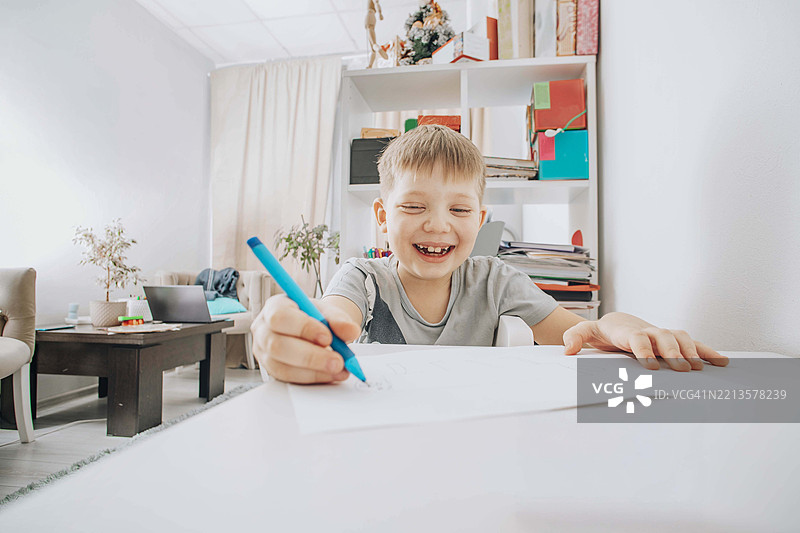 微笑的男孩专注于在明亮的房间里学习桌上绘画，早期教育的概念图片素材