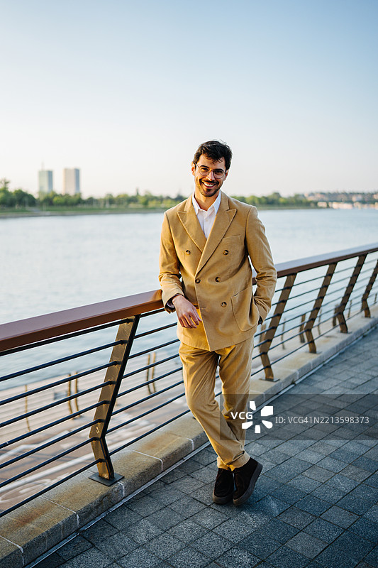 微笑的商人靠在城市河边的栏杆上图片素材