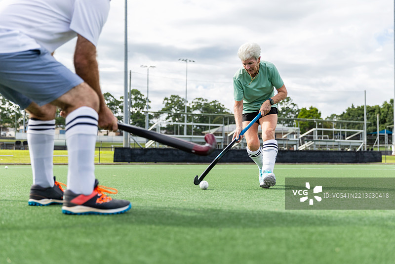 男性曲棍球运动员与一位资深女性运动员争夺球权图片素材