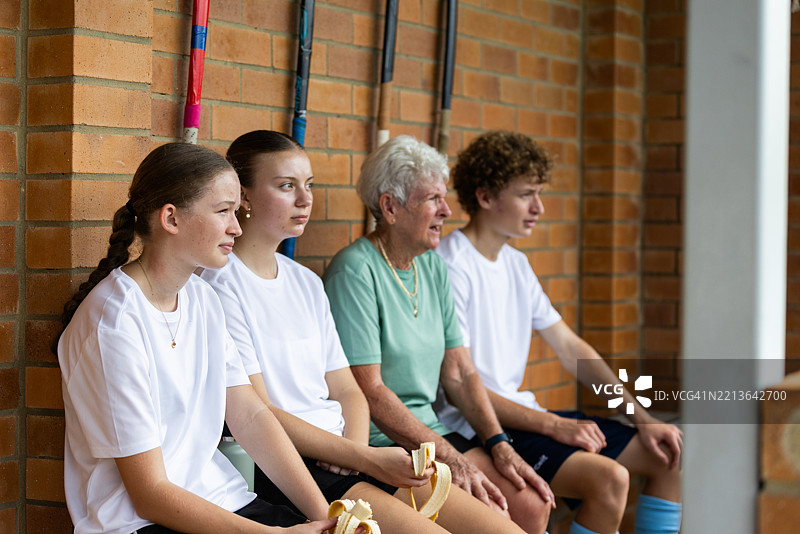 不同年龄的曲棍球队队友在替补席上一起观看比赛图片素材