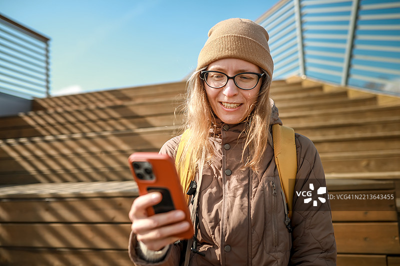当地旅行为生活注入活力，一位穿着外套和眼镜的女性在阳光明媚的蓝天下进行视频通话。图片素材