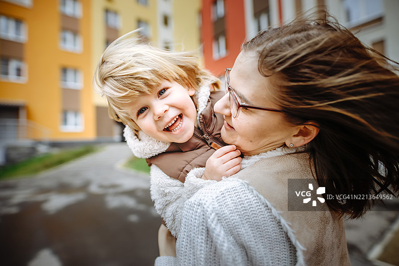 在新城区的欢乐氛围中，一位年轻母亲温柔地将儿子抱在怀里旋转，享受着新鲜的空气。图片素材