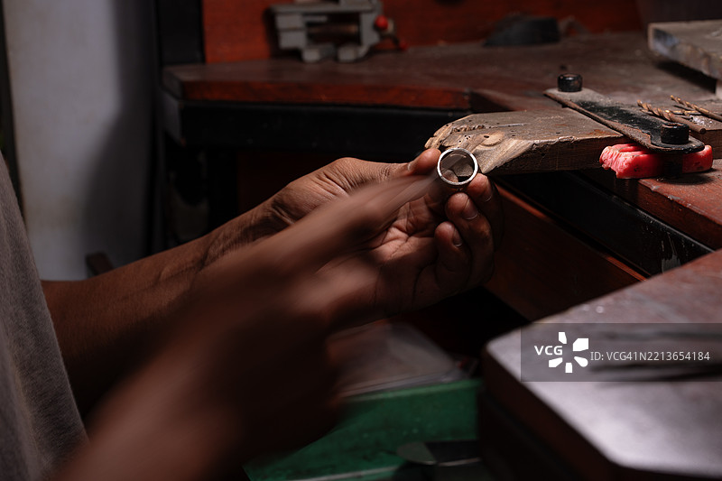珠宝匠的手在木制工作台上仔细打磨银戒指的特写镜头图片素材