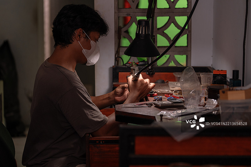 男性珠宝匠在珠宝工作室中使用旋转工具对银戒指进行细致打磨的侧面视图图片素材