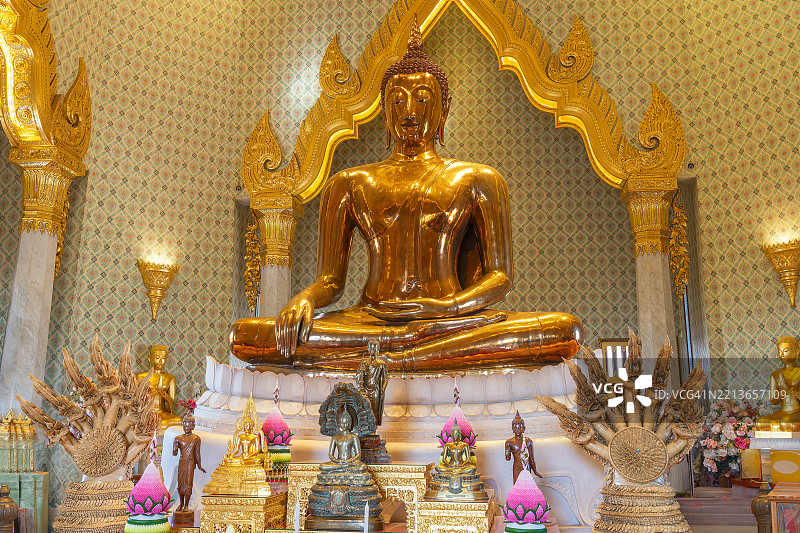 曼谷一座华丽佛教寺庙内坐着金色佛像，周围环绕着较小的佛像和供品，展示了泰国佛教丰富的文化遗产。泰国曼谷图片素材
