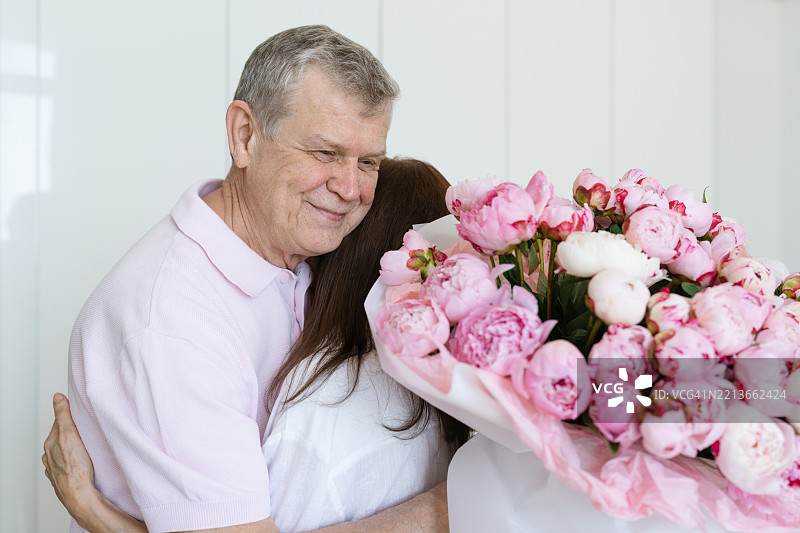 一位老年男子拥抱着一位女性，送给她鲜花。图片素材