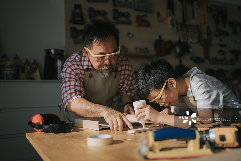 亚洲华裔祖父在家里的工作坊教孙子木工技艺图片素材