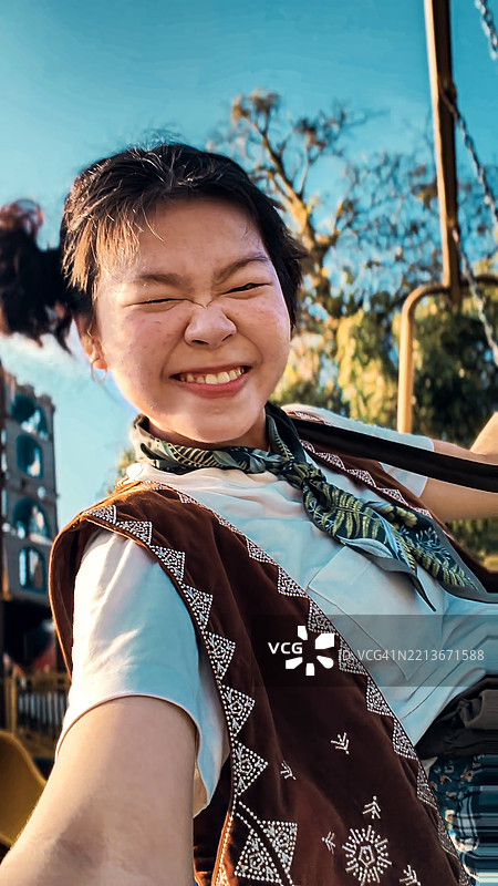 快乐的年轻亚洲女性在游乐场秋千上欢呼雀跃图片素材