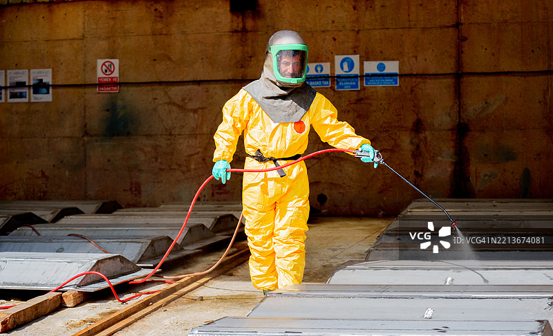 穿着防护服的危险品处理工正在消毒工业金属表面图片素材