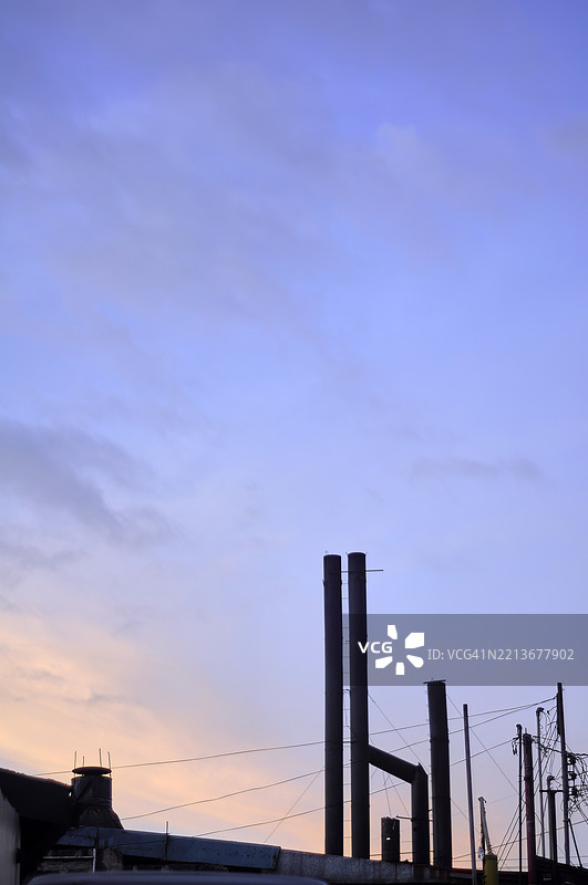 工厂烟囱的轮廓映衬在绚丽的日落色彩中。图片素材