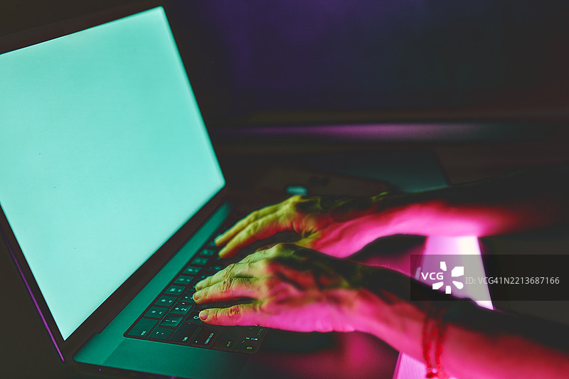 手在笔记本电脑上打字，周围被鲜艳的霓虹色彩照亮图片素材