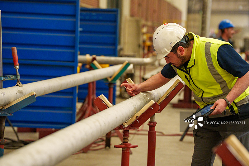 技术员在工业车间使用游标卡尺测量管道直径图片素材