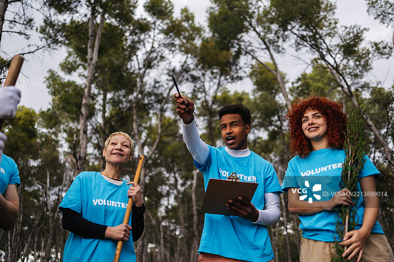 志愿者在森林中指点并讨论植树造林策略图片素材