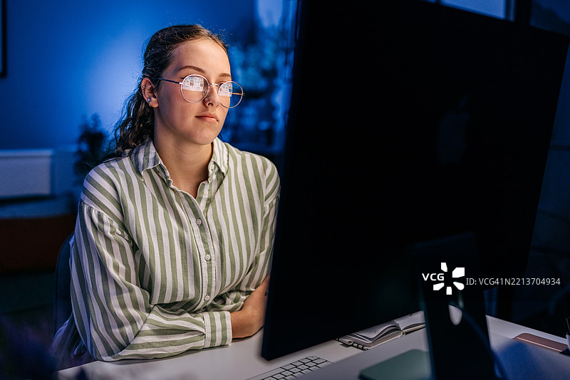 美丽的女性在夜晚的家中办公室使用台式电脑图片素材