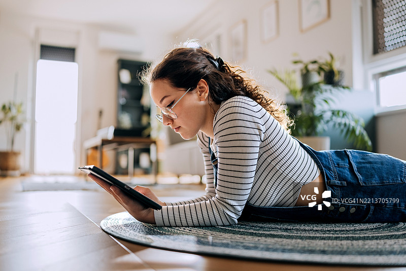 年轻女性在家中躺在地板上使用平板电脑图片素材