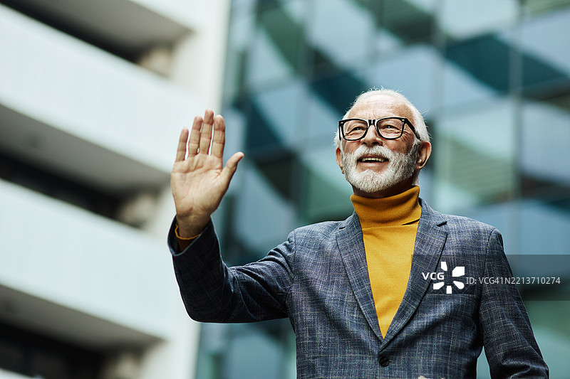 一位英俊的退休老人正在下午散步时向邻居打招呼。图片素材