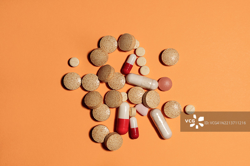 各种药丸和胶囊在橙色背景上形成生动的排列图片素材