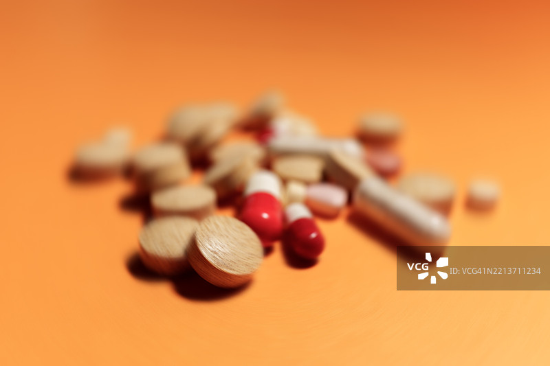 各种药丸和胶囊堆成一堆，背景为橙色图片素材