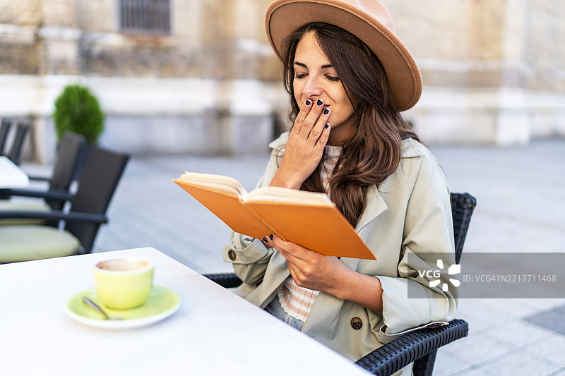 年轻女性在户外咖啡馆阅读一本令人惊讶的书图片素材
