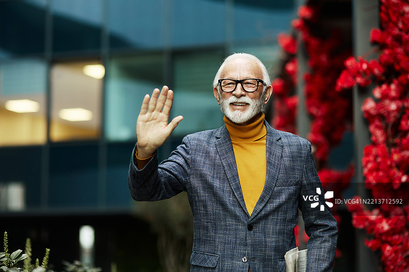 一位英俊的退休老人在下午散步时向邻居打招呼。图片素材