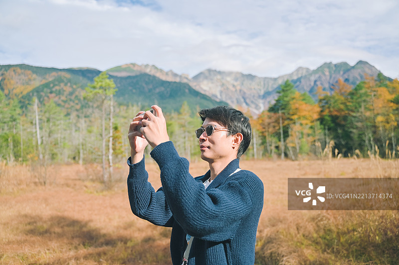 愉快的亚洲男子在长野的上高地拍摄秋季山脉风景，天空多云。图片素材