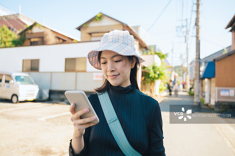 身穿休闲服的Z世代日本女性游客，在日本一个宁静的小镇上使用智能手机。图片素材